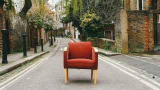 fauteuil rouge au milieu d'une rue, sol gris, murs en pierres rouge à droite, poteaux noir à gauche